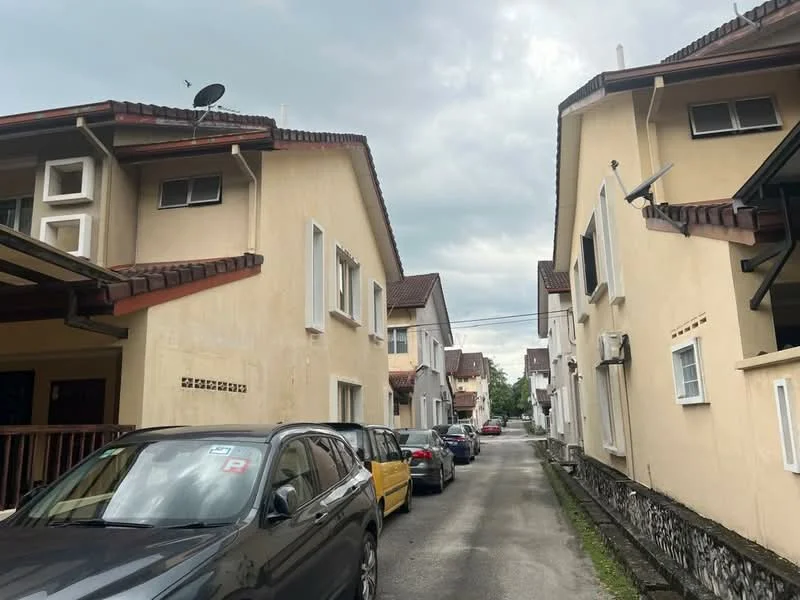 Exterior type: linked terrace house; features: yellow painted facade, two-storey buildings, gabled roof, satellite dishes on roof, driveway with parked cars, narrow access road, visible windows, decorative stone cladding at base; style: traditional.