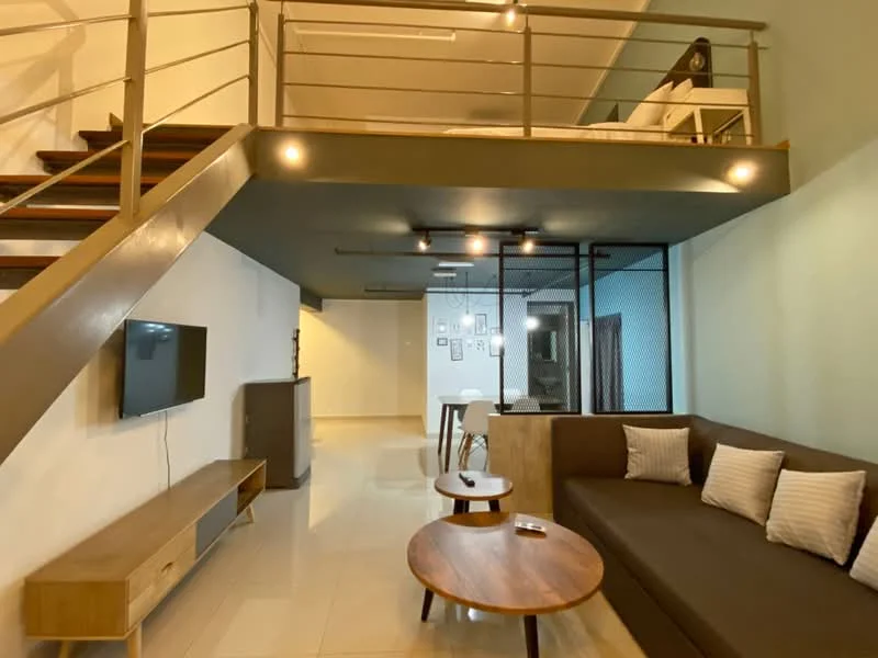 Living features: L-shape sectional sofa in dark brown, two round wooden coffee tables, wall-mounted TV, TV console in light wood, white walls, recessed downlights, polished tile flooring, open-plan layout, glass partition wall, staircase with metal railing; style: modern. Room features: light wood cabinetry, white walls, recessed downlights.