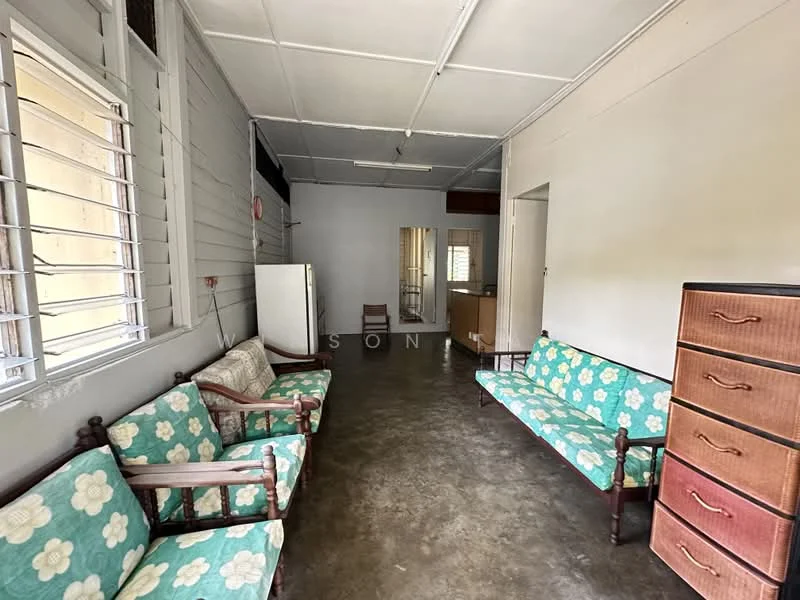 Living features: green floral patterned sofas, wooden armchairs, concrete flooring, white painted walls, large windows with metal grilles, mirror on wall, refrigerator, wooden chest of drawers; style: traditional.