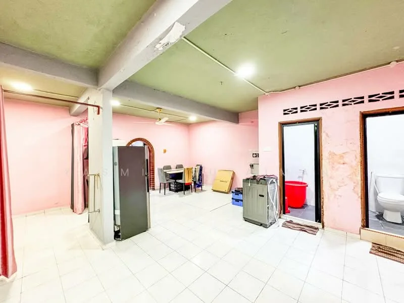 Room features: pink painted walls, white tiled flooring, exposed concrete ceiling, ceiling fan, fridge, dining table with chairs, laundry area with washing machine, two doors leading to separate rooms, red storage container, bathroom door visible.
