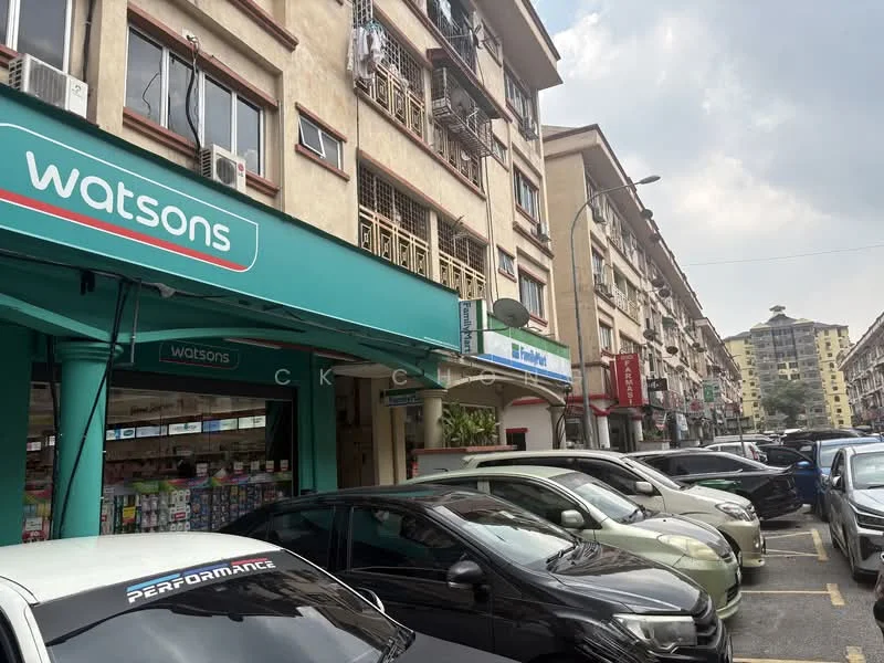 Exterior type: low-rise apartment block; features: commercial ground floor with retail shops, multiple storeys, balconies on upper floors, visible air conditioning units, parking area with multiple cars, signage for Watsons, street view, urban context with surrounding buildings; style: modern.
