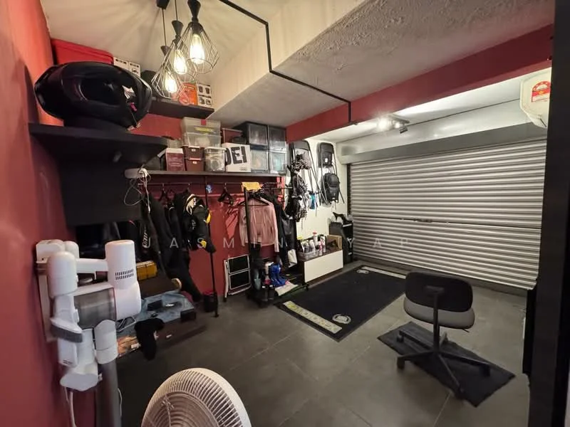 Room features: red painted walls, black shelving unit, hanging storage for clothing, various helmets displayed, grey tiled flooring, overhead pendant lighting, roller shutter door, black office chair, fan, storage boxes, white storage unit, black mat on floor; style: modern.