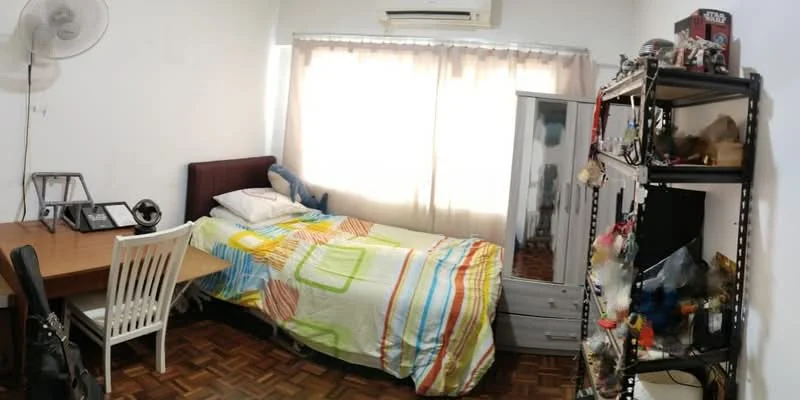 Bedroom features: single bed with colorful bedding, wooden flooring, white painted walls, large window with sheer curtains, air conditioning unit, study desk with chair, full-length mirror, open shelving unit with decorative items, table lamp.