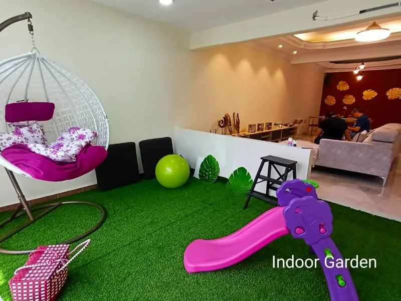 Room features: hanging egg chair with floral cushions, artificial grass flooring, pink slide, green exercise ball, black stools, decorative leaves, sofa in light color, wall with floral decor, recessed ceiling lights; style: modern.