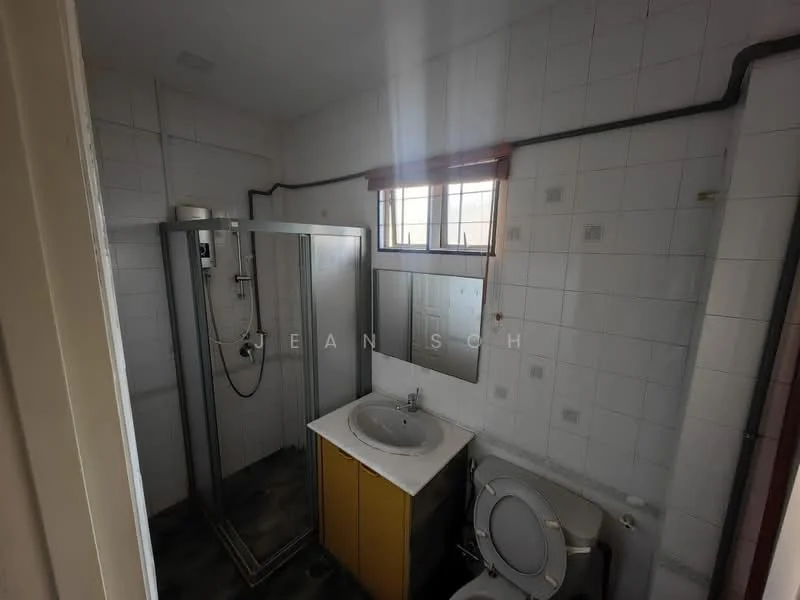 Bathroom features: white tiled walls, grey tiled flooring, shower cubicle with glass door, chrome shower head, single-sink vanity with yellow cabinet, mirror above vanity, toilet, window with grid pattern, plumbing pipes visible.