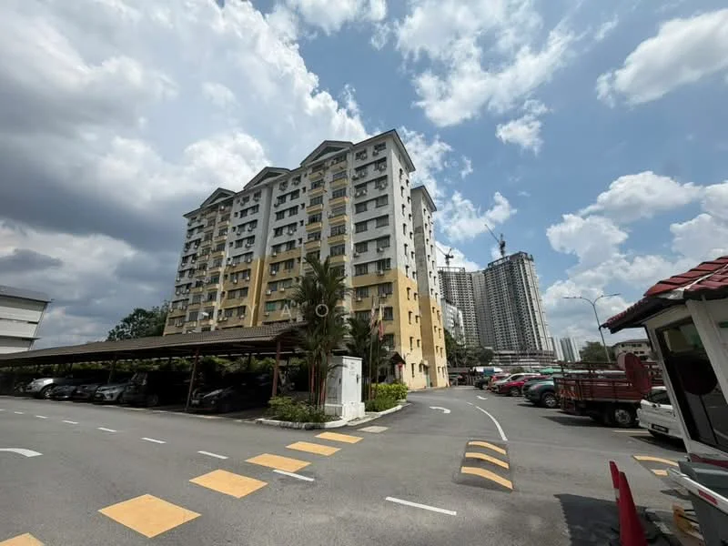Exterior type: low-rise apartment block; features: yellow painted facade, 5-storey building, covered parking area, manicured landscaping, palm trees, surrounded by urban development, adjacent to construction site, driveway with interlocking pavers; style: modern.
