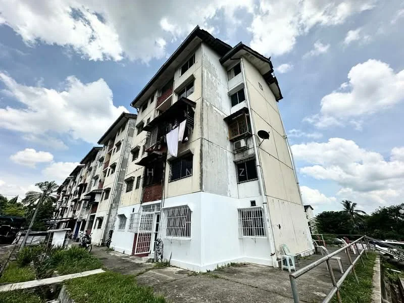 Exterior type: low-rise apartment block; features: white painted facade, balconies with laundry hanging, ground-level access, concrete walkway, metal railings, multiple storeys, visible windows, surrounding greenery; style: traditional.