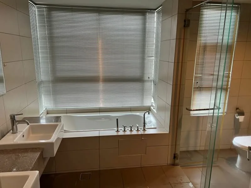 Bathroom features: freestanding bathtub, glass shower enclosure, double-sink vanity with stone countertop, chrome basin mixer faucets, white tiled walls, grey tiled flooring, blinds on windows, toilet, wall-mounted mirror; style: modern.