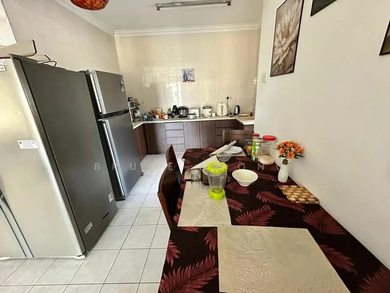 Kitchen features: grey stainless-steel fridge, wood cabinetry, white tiled backsplash, ceramic tile flooring, kitchen island with seating, table with floral tablecloth, various kitchen appliances visible, decorative flowers in vase, wall-mounted artwork, multiple countertop appliances; style: modern.