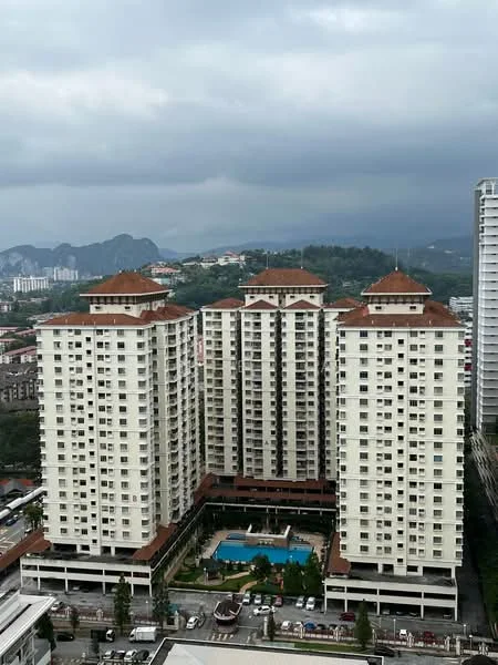 Exterior type: high-rise condominium; features: white painted facade, red tiled roof, multiple storeys, balconies on upper floors, landscaped pool area, surrounded by greenery, parking deck at ground level, urban context with nearby buildings, mountain view in background; style: modern.
