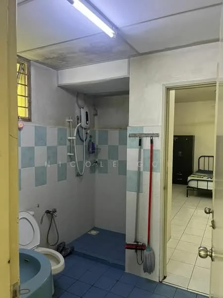 Bathroom features: toilet, shower area with wall-mounted showerhead, blue tiled flooring, light blue and white tiled walls, mirror, wall-mounted soap dispenser, cleaning supplies (broom and mop), window for natural light, door leading to another room.