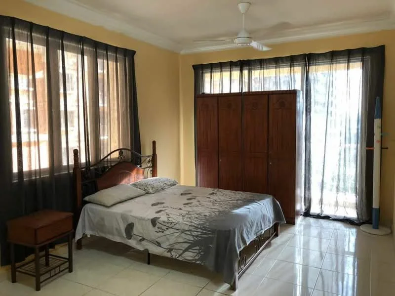 Bedroom features: queen-size bed, bedding with floral pattern, wooden bedside table, 4-door wooden wardrobe, floor-to-ceiling windows, black sheer curtains, white painted walls, glossy tile flooring, ceiling fan.