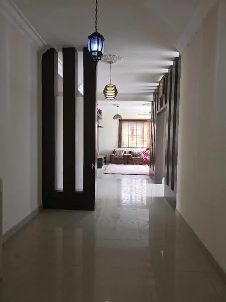 Room features: white painted walls, glossy tile flooring, ceiling with recessed downlights, hanging pendant light, decorative wall paneling, large window with natural light, neutral color scheme, open layout, living area visible in background; style: modern.