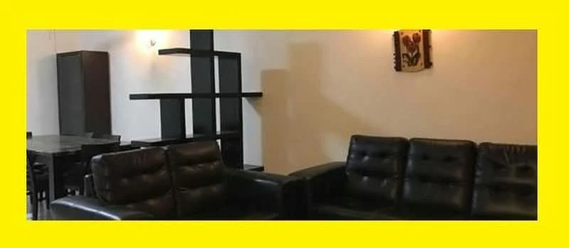 Living features: black leather sofa with tufted design, black armchair, black shelving unit with geometric design, wall-mounted light fixture, decorative wall art, dark wooden dining table, four dining chairs, white painted walls, dark flooring; style: modern.