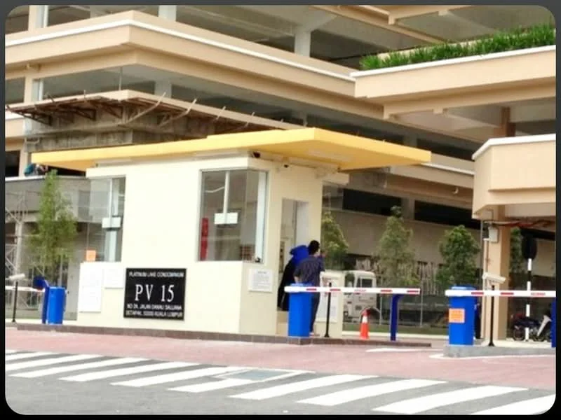 Exterior features: guard house at entrance, security boom gate, paved driveway, landscaped greenery, signage with property name, surrounded by construction scaffolding; style: modern.
