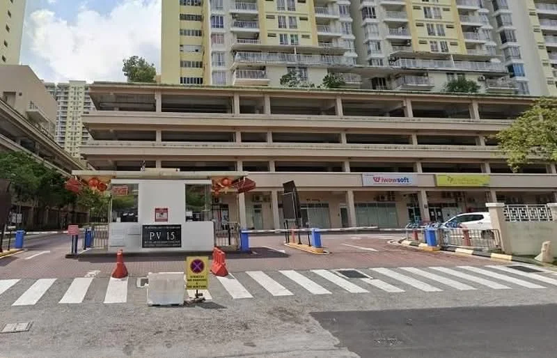 Exterior type: multi-storey car park; features: multi-storey structure, open-air parking lot, paved driveway, entrance with security gate, visible signage for businesses, surrounded by residential buildings, landscaped areas with trees, marked pedestrian crossing; style: modern.