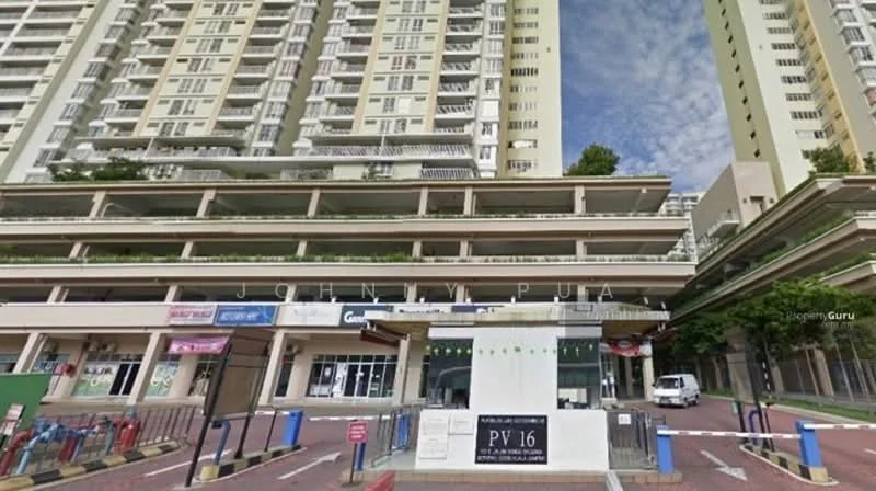 Exterior type: high-rise condominium; features: glass curtain wall, multiple recessed balconies, green landscaping on balconies, commercial units at ground level, driveway with interlocking pavers, security guard house at entrance, visible signage for businesses, surrounded by mature greenery; style: modern.