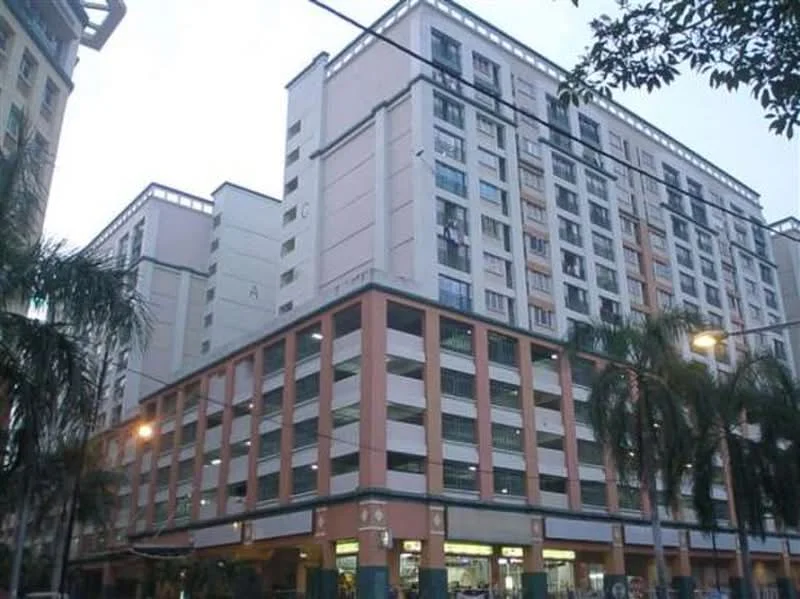 Exterior type: mid-rise condominium; features: light pink painted facade, concrete structure, multiple storeys, balconies visible on upper floors, parking deck at ground level, palm trees in foreground, street lighting, windows with grills; style: modern.