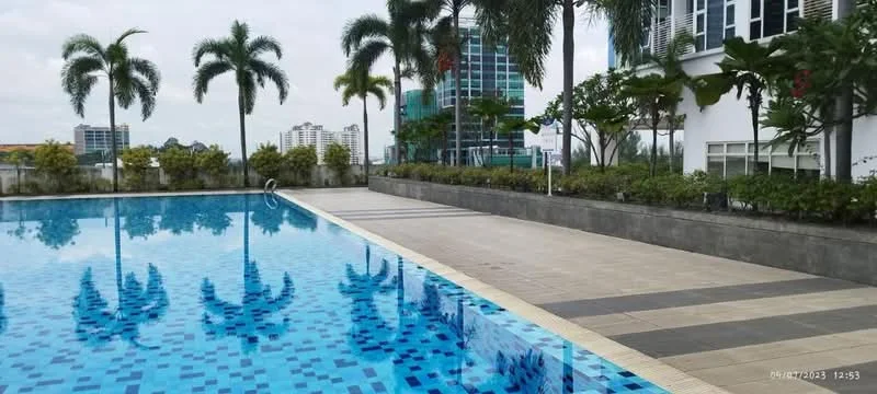 Exterior type: swimming pool deck; features: infinity pool, tiled pool surface with blue mosaic pattern, surrounded by palm trees, landscaped garden area, concrete pool deck, city skyline in background, lounging area with pavers; style: modern.