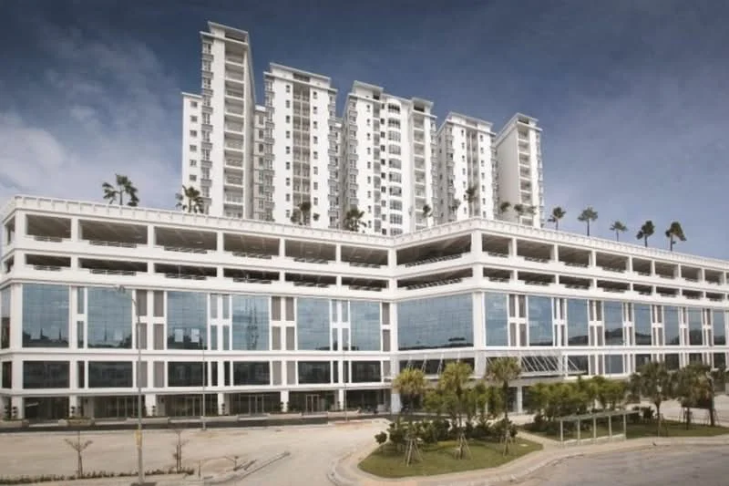 Exterior type: high-rise condominium; features: glass curtain wall, white painted facade, recessed balconies, multiple storeys, palm trees on roof, manicured landscaping, large windows, open-air parking area; style: modern.