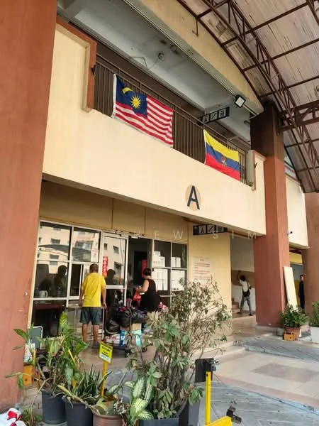 Exterior type: shophouse; features: two-storey building, entrance with glass doors, overhang roof, Malaysia and Venezuela flags displayed, potted plants at entrance, signage above entrance, open space in front of building; style: modern.