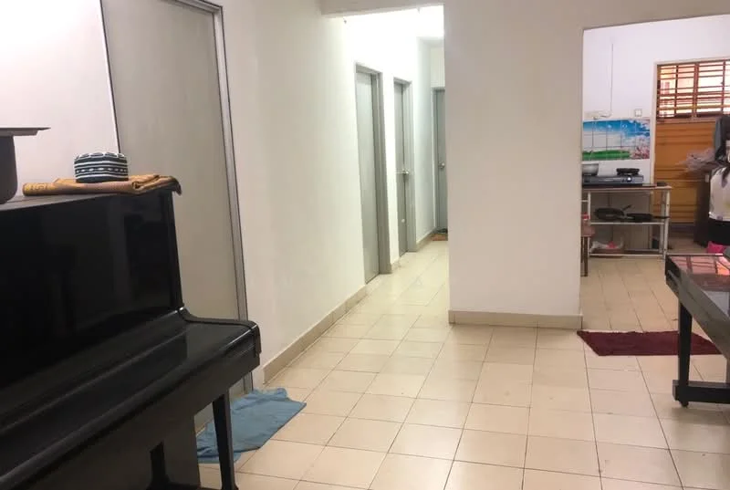 Room features: white painted walls, tile flooring, piano, multiple doors leading to other rooms, kitchen area visible in background, light fixtures on ceiling, area rugs, open layout.