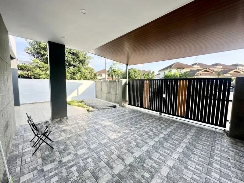 Exterior type: car porch; features: paved flooring with patterned tiles, covered area with wooden ceiling, black wooden slatted gate, concrete wall, landscaped area with greenery, open space, surrounded by residential houses; style: modern.