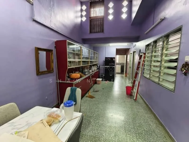 Room features: purple painted walls, green terrazzo flooring, large glass display cabinet, wooden framed mirror, metal ladder, window with horizontal slats, ceiling with decorative cut-outs, dining table with marble top, plastic water jug, red bucket.