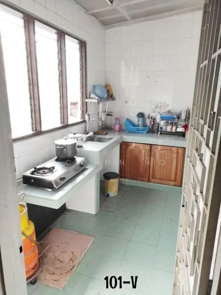 Kitchen features: white tiled walls, green vinyl flooring, single-bowl stainless-steel sink, chrome pull-down faucet, built-in countertop with storage, wood cabinetry, gas stove with 4 burners, exhaust hood, window with metal grilles, kitchen utensils on countertop, trash bin, floor mat.