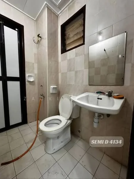 Bathroom features: white ceramic toilet, single-sink vanity with chrome faucet, framed mirror, tile flooring, beige wall tiles, grey accent wall tiles, shower hose attachment, window for natural light, wall-mounted soap dispenser.