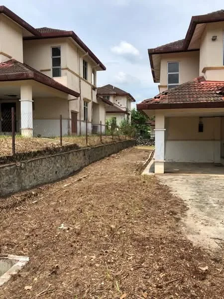 Exterior type: semi-detached house; features: two-storey building, red tiled roof, cream painted facade, fenced yard, gravel landscaping, concrete driveway, adjacent houses, open space on side, mature trees in background; style: modern.