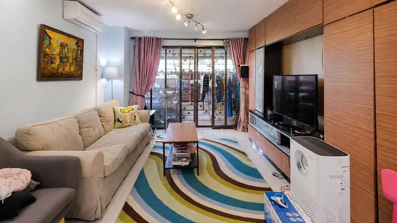 Living features: beige fabric sofa, grey fabric armchair, wood coffee table, area rug with wavy pattern in multiple colors, wall-mounted TV, TV console, built-in wooden cabinetry, floor-to-ceiling sliding glass door, curtains in pink, air conditioning unit, decorative painting on wall, ceiling track lighting; style: modern.