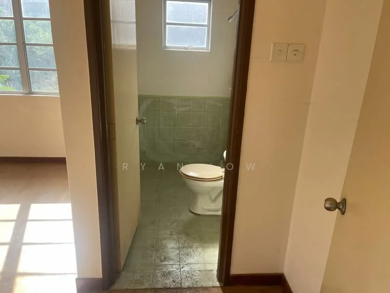 Room features: white painted walls, green tiled flooring, one-piece toilet, window for natural light, door leading to another room, light switch on the wall, door handle, visible plumbing fixtures.