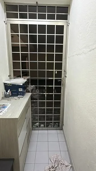 Room features: white painted walls, grey tiled flooring, metal security door with grid pattern, wooden cabinet with drawers, stack of magazines on cabinet, floor mat, visible shoes on the floor.