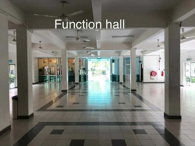 Room features: tiled flooring with black and white pattern, high ceiling, multiple ceiling fans, large windows for natural light, open layout, fire extinguisher mounted on wall, double glass doors leading outside, white painted walls, fluorescent lighting, visible reception area in background; style: modern; view: garden.
