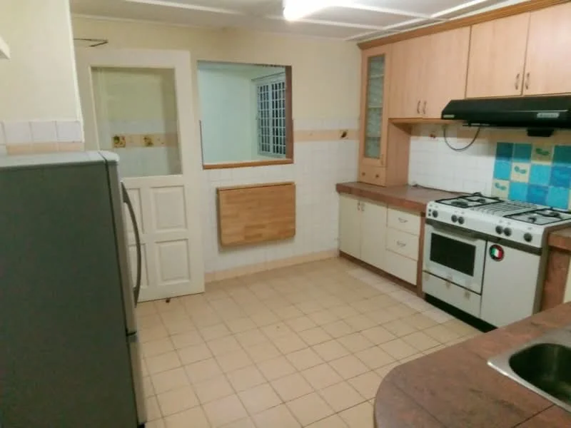 Kitchen features: stainless-steel fridge, built-in oven, 4-burner gas hob, single-bowl stainless-steel sink, chrome pull-down faucet, laminate countertop, white cabinetry, tile backsplash with blue accents, ceramic tile flooring, wall-mounted range hood, wooden cutting board, window with grid pattern.