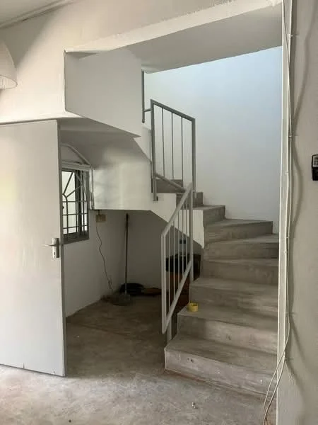 Room features: spiral staircase, concrete flooring, white painted walls, window with metal grille, door with handle, exposed electrical wiring, light fixture on ceiling; style: minimalist.