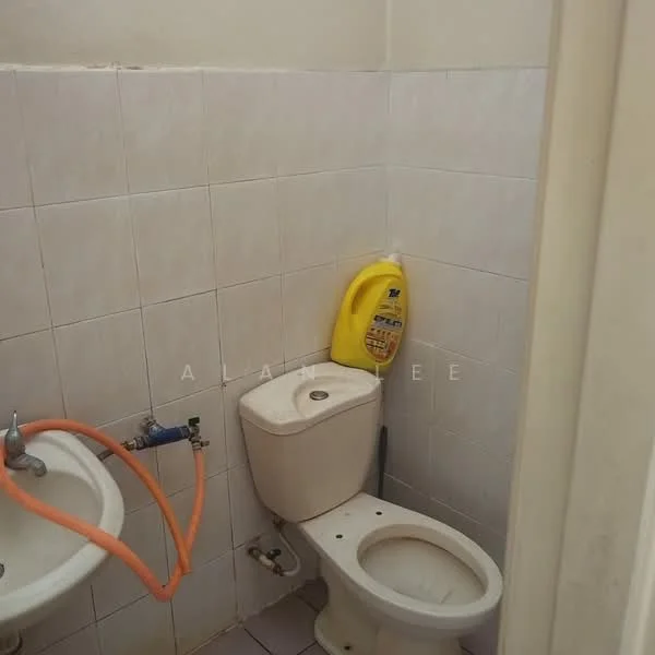 Bathroom features: white tiled walls, white ceramic floor tiles, one-piece toilet, sink with wall-mounted faucet, orange hose, yellow cleaning product, exposed plumbing, small space layout.