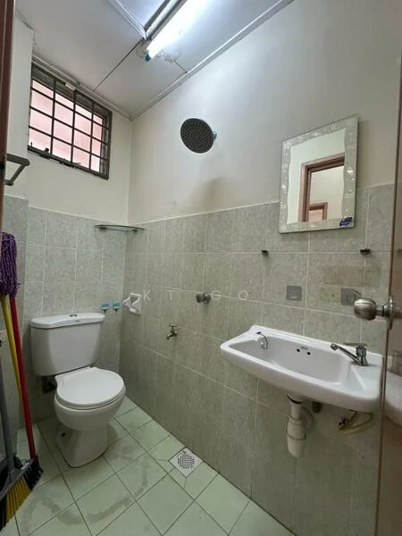 Bathroom features: white ceramic toilet, single-sink vanity with wall-mounted faucet, framed mirror, shower head, tiled walls in light grey, light green floor tiles, wall-mounted shelf, exhaust fan, window for natural light, cleaning supplies visible.