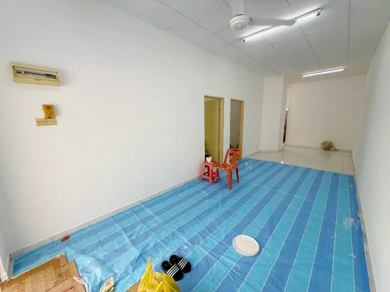 Room features: white painted walls, tile flooring, 5-blade ceiling fan, air conditioning unit on wall, blue plastic sheet on floor, two doorways leading to other rooms, plastic chairs, round plate on floor, yellow plastic bag.