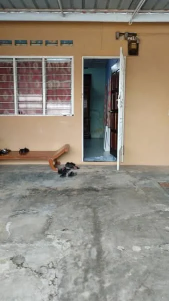 Room features: concrete flooring, brown painted walls, white door, window with metal grille, curtains, shoes on the floor, wooden bench, light fixture on the wall.