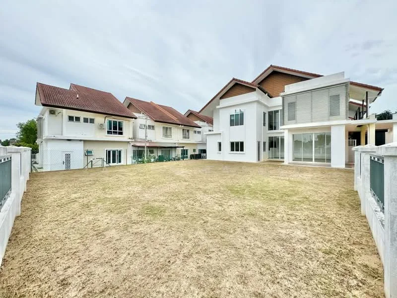 Exterior type: detached bungalow; features: white painted facade, flat roof, two-storey structure, manicured lawn, surrounded by other residential buildings, large open yard area, multiple windows, balcony on upper floor, driveway, fenced perimeter; style: modern.