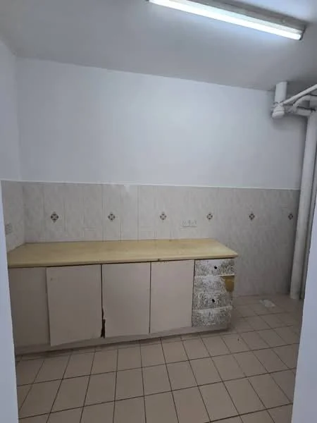 Kitchen features: light-colored cabinetry, wooden countertop, white tiled backsplash, cream tiled flooring, wall-mounted fluorescent lighting, sink plumbing visible, no visible appliances, neutral wall color.