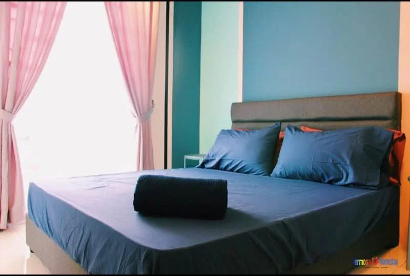 Bedroom features: king-size bed with blue bedding, upholstered headboard, two blue pillows, rolled blue towel on bed, light wood bedside table, floor-to-ceiling window, sheer curtains in light pink, accent wall in teal, white walls, laminate flooring; style: modern; view: city.