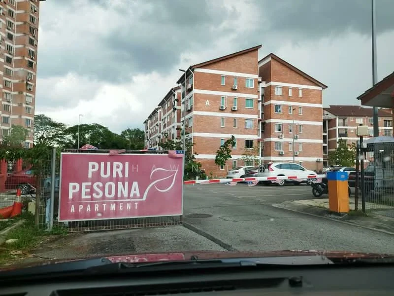Exterior type: low-rise apartment block; features: red brick facade, multiple storeys, surrounded by greenery, parking area visible, entrance gate, signage for Puri Pesona Apartment; style: modern.