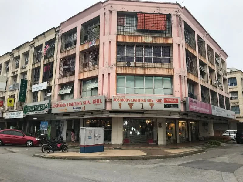 Exterior type: shophouse; features: pink painted facade, three-storey building, ground floor retail space, balconies on upper floors, metal grilles on windows, signage for businesses, corner lot, asphalt parking area, surrounded by other commercial buildings; style: traditional.