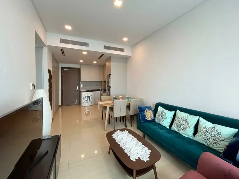 Living features: green fabric sofa with cushions, wooden coffee table, TV console, wall-mounted TV, dining table with four chairs, recessed ceiling lights, cream tiled flooring, open-plan layout to kitchen, washing machine in kitchen area, neutral painted walls, air conditioning unit; style: modern. Kitchen features: built-in kitchen cabinets, stainless-steel sink, gas hob, built-in oven, microwave, refrigerator, countertop space, tile backsplash; style: modern.