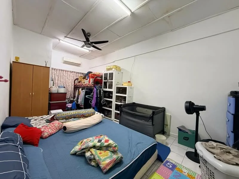 Bedroom features: queen-size bed with blue bedding, colorful patchwork quilt, ceiling fan, white painted walls, tile flooring, built-in wardrobe with wooden doors, clothes rack, laundry basket, black portable fan, white storage unit, window with sheer curtains, play mat with numbers, crib, dressing table with mirror.