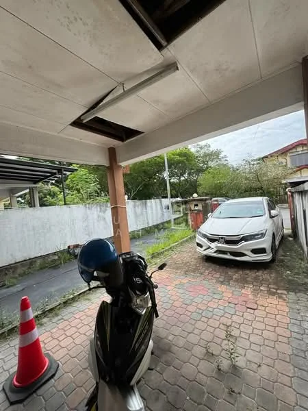 Exterior type: car porch; features: paved driveway with interlocking pavers, covered car porch, white painted walls, overhead lighting fixture, motorcycle parked, red and white traffic cone, greenery in background, fenced perimeter; style: modern.