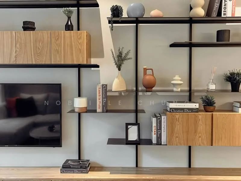 Living features: wall-mounted TV, wooden shelving unit with black metal frame, decorative vases, books on shelves, houseplants in pots, neutral wall color, wooden console table, decorative objects; style: modern.